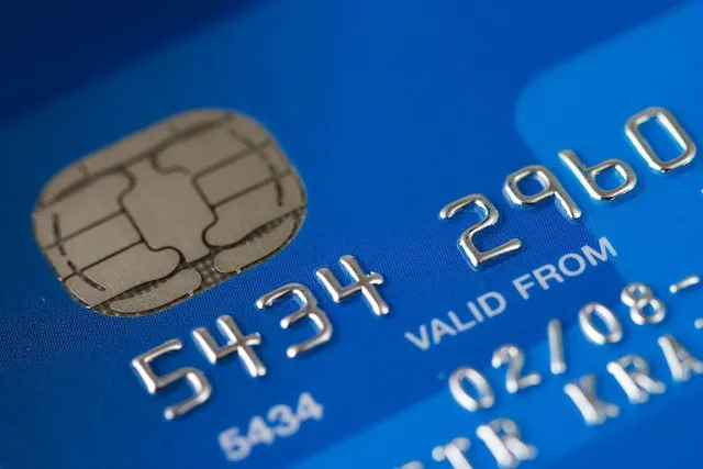 Close-up of a blue credit card showing its gold EMV chip, embossed card number and valid-from date