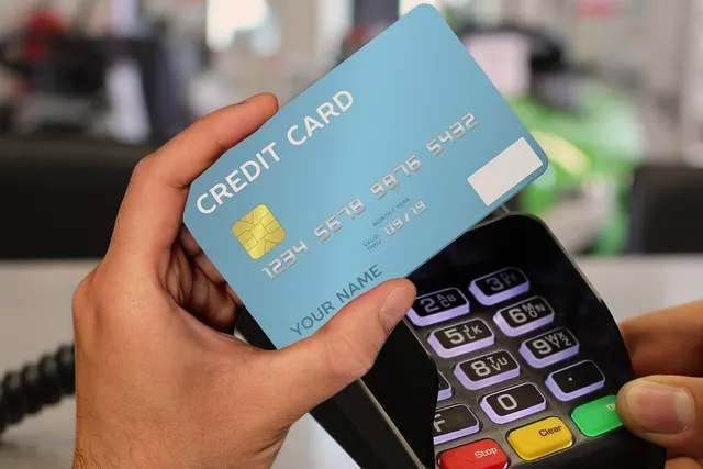 Customer holds a blue credit card over a card payment terminal as a cashier holds the keypad at a store counter