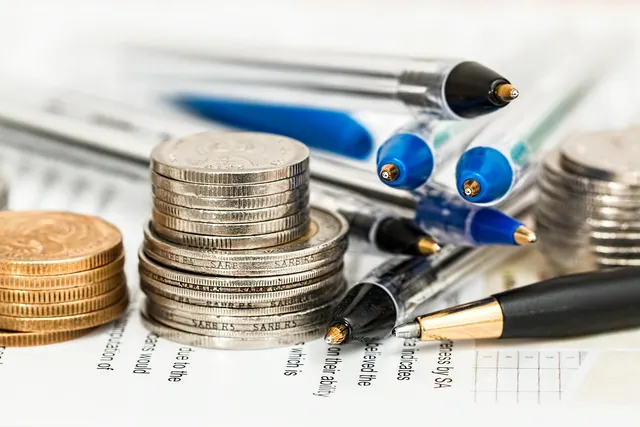 Stacks of silver and copper coins beside blue and black ballpoint pens resting on a printed financial document