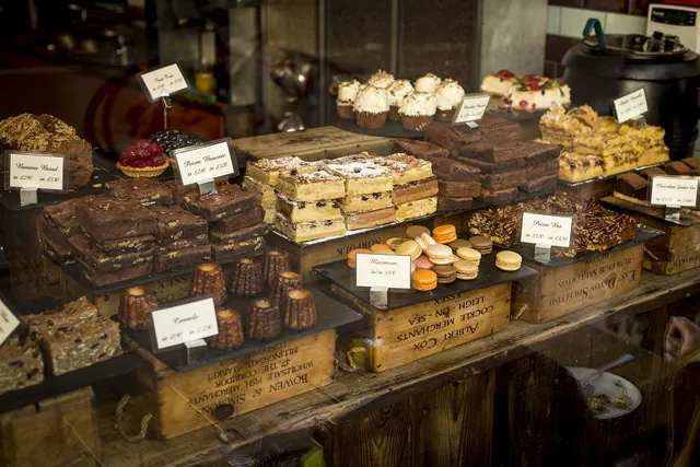 Bakery window display of brownies, macarons, cupcakes and tray bakes on wooden crates with handwritten price cards