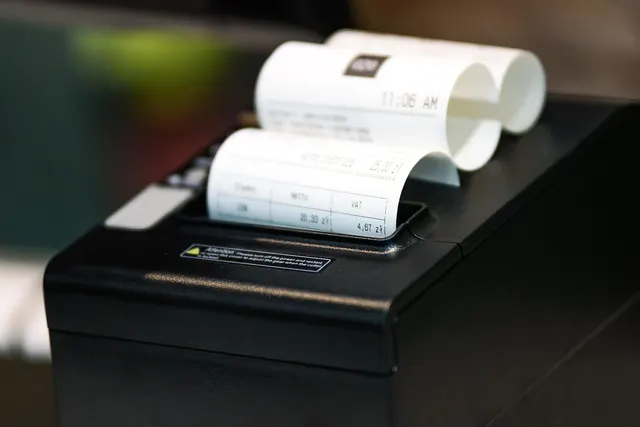 Black thermal receipt printer issuing paper receipts that show net and VAT amounts and a time stamp