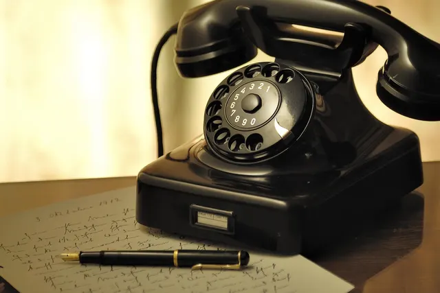 Vintage black rotary telephone on a wooden desk beside a handwritten letter and a fountain pen