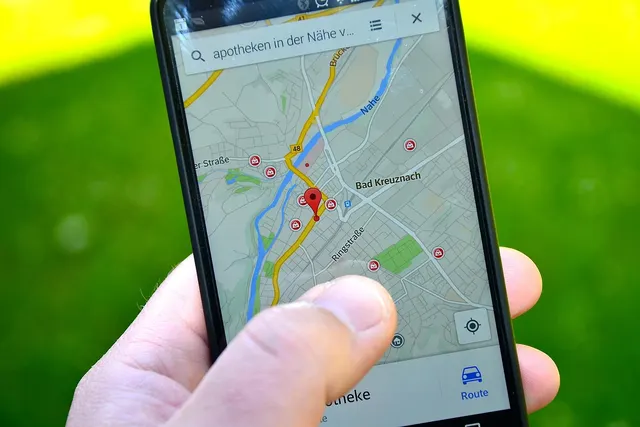 Hand holding a smartphone showing a map app with a red location pin over city streets, green lawn behind
