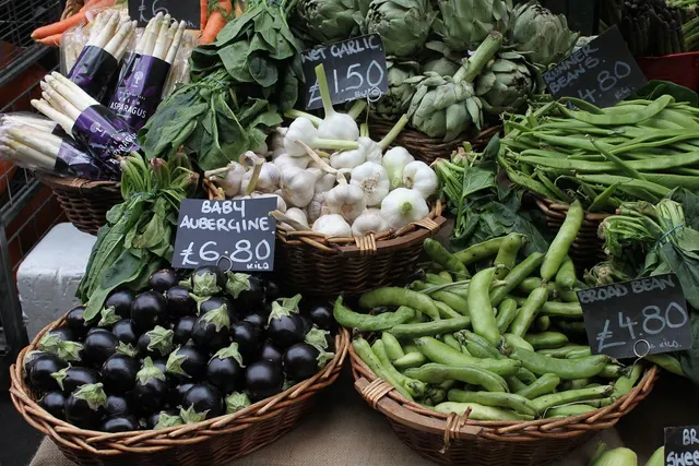 Wicker baskets of baby aubergines, broad beans, wet garlic, artichokes and asparagus with chalkboard prices at a market stall