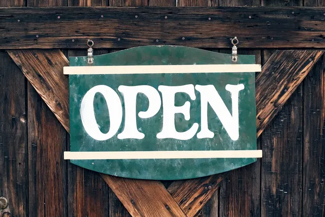 Green hand-painted OPEN sign hanging on a weathered wooden barn-style door