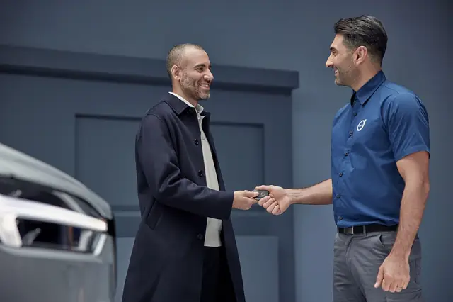 Salesman handing car keys to a smiling customer by a car