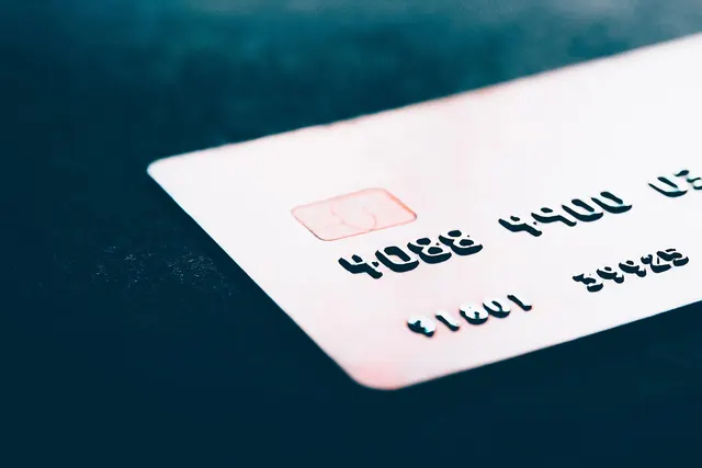 Close-up of a white payment card with an EMV chip and embossed numbers resting on a dark surface