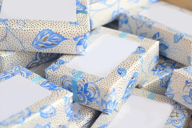 Stack of small packages wrapped in blue floral and gold-dotted paper, each with a blank white label and teal tape