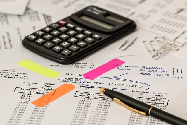 Calculator, pen, paper clips and sticky notes on printed investment tables with a note about tax implications