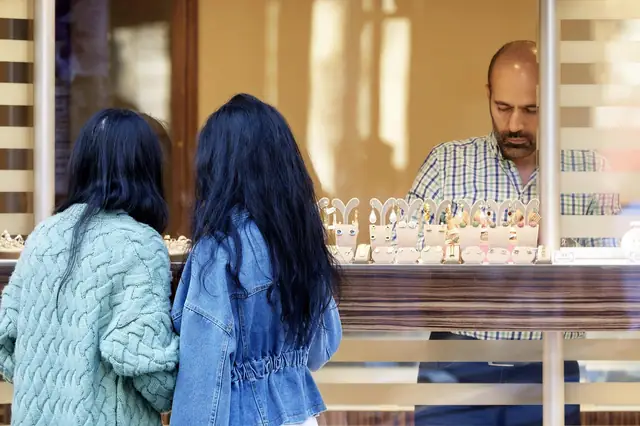 Two shoppers looking at a jewelry counter while a jeweler waits