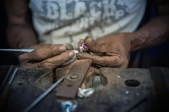 Jeweler's hands setting a gemstone into a ring at a workbench
