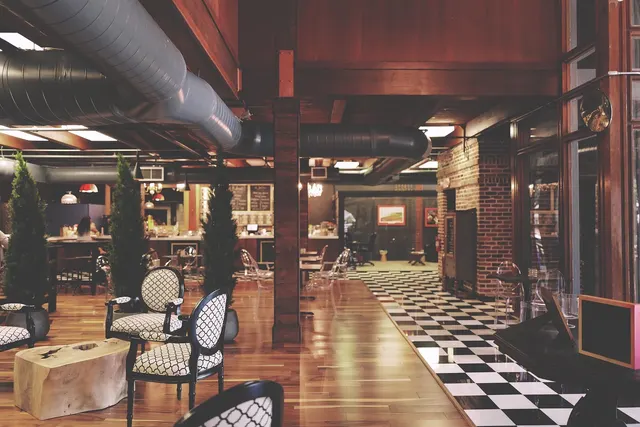 Empty cafe bar interior with wood floors, black-and-white checkered tile, patterned chairs and exposed ductwork