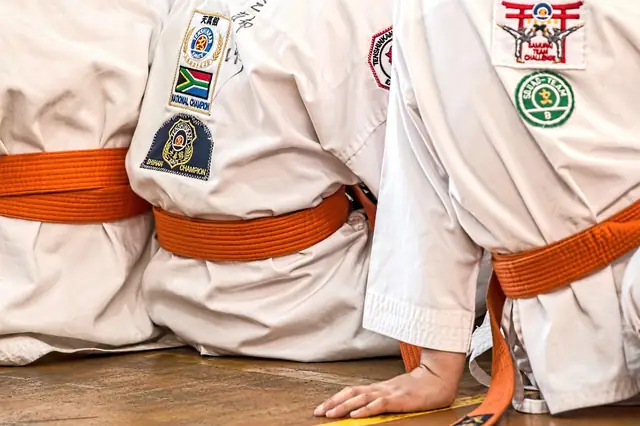 Martial arts students in white uniforms and orange belts kneeling