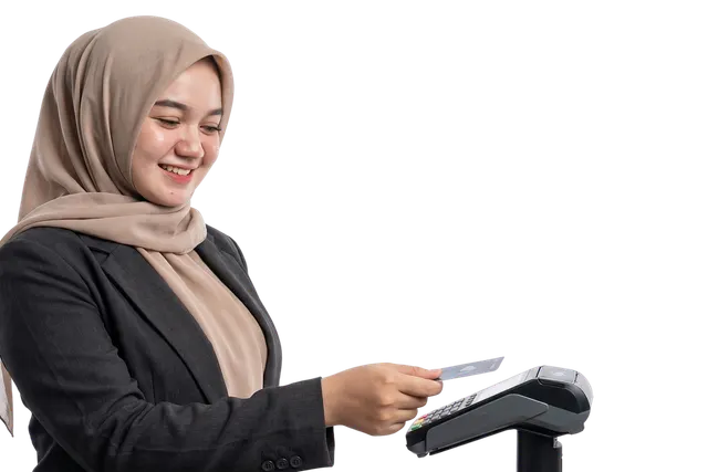 Smiling woman in a beige hijab and dark blazer tapping a card on a countertop payment terminal against a black backdrop