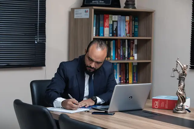 Lawyer in a suit signing papers at a desk with a laptop