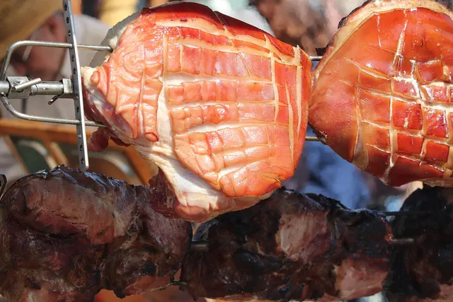 Scored, crackling-skinned pork legs and darker roasted pork turning on rotisserie spits at an outdoor roast
