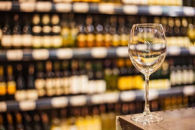 Empty wine glass on a counter in front of blurred shelves of wine and liquor bottles in a retail store