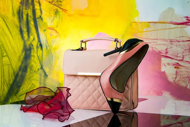 Blush pink quilted handbag with a pink and black stiletto heel and red ruffled scarf against an abstract painted backdrop