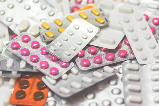Pile of blister packs holding pink, yellow and white pills and capsules, with an orange pack in the corner