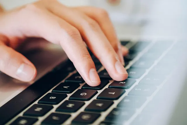 Close-up of a hand typing on a silver laptop keyboard with dark keys