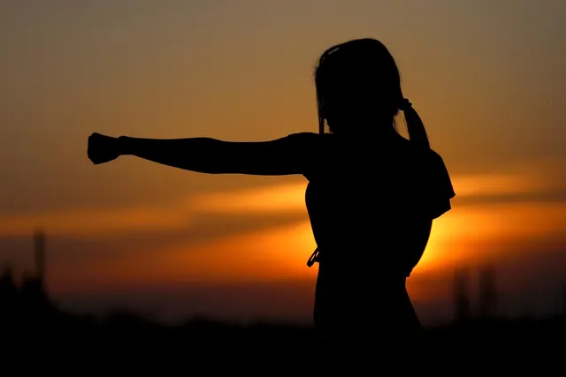 Silhouette of a woman with a ponytail throwing a straight punch against an orange sunset sky