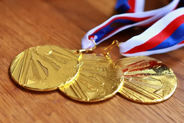 Three gold medals with red, white and blue ribbons lying on a wooden table