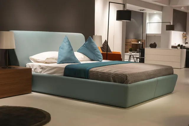 Upholstered teal bed with mattress, gray throw and blue pillows on display in a furniture store showroom