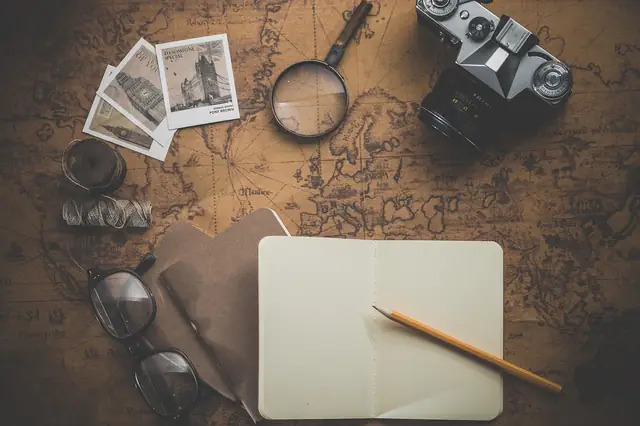 Vintage map with camera, magnifier, photos and notebook laid flat