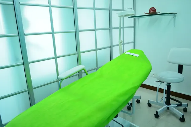 Med spa treatment room with a reclining chair under a lime green cover, a magnifying lamp and a rolling stool by frosted glass