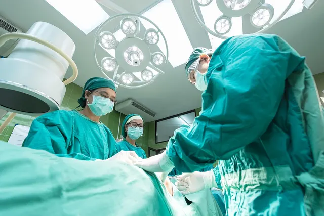 Surgical team in teal scrubs, caps and masks operating beneath bright surgical lights in a hospital operating room