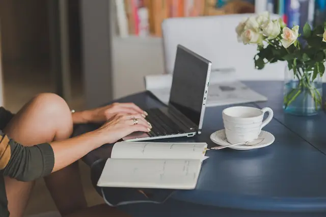 Woman typing on a laptop beside coffee and flowers at a table