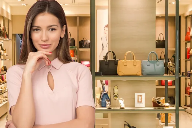 Woman in a pink top poses thoughtfully in a boutique with handbags and high-heeled shoes displayed on shelves