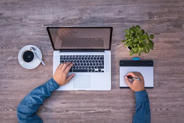 Overhead view of hands using a laptop and drawing tablet on wood