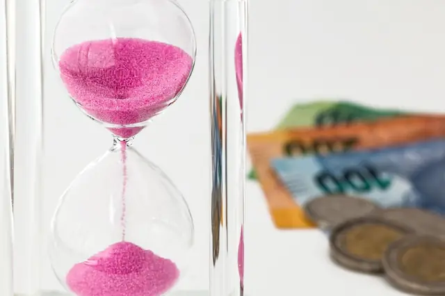 Pink sand hourglass beside banknotes and stacked coins