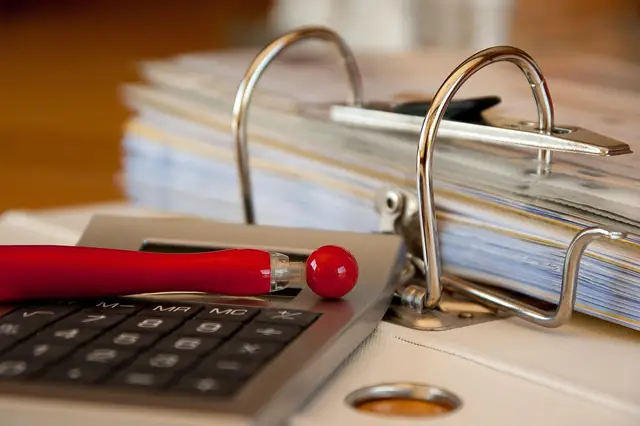 Open ring binder of papers beside a calculator and red pen