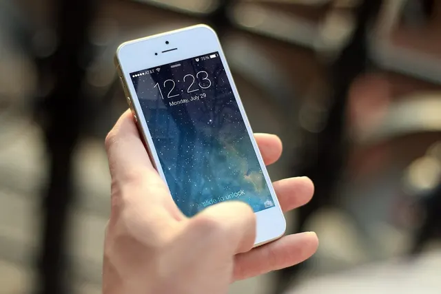 Hand holding a white smartphone showing a lock screen with the time 12:23 and a starry blue wallpaper