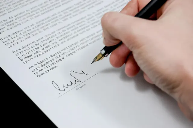 Close-up of a hand signing a printed document with a fountain pen on the signature line