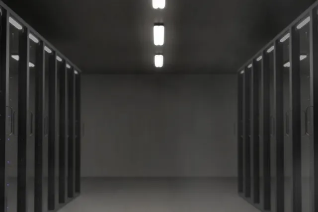 Dimly lit data center aisle lined with rows of black server racks with blue status lights under ceiling lamps