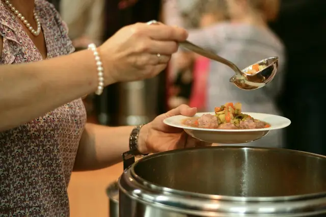 Volunteer ladling food onto a plate from a large pot