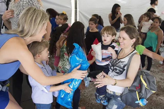 Volunteer hands a blue gift bag to a young boy at a crowded charity event under a white tent as families wait