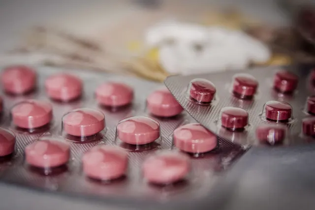 Close-up of pink and dark red tablets in silver blister packs on a table, with a soft blurred background