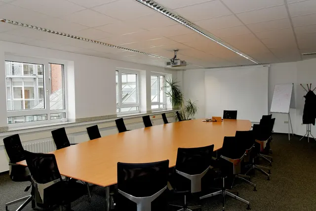 Empty conference room with a long wooden table, black office chairs, a projector screen and a flip chart