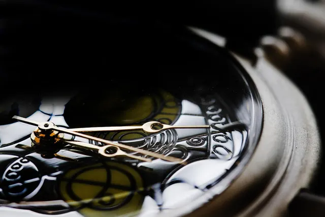 Close-up of a luxury watch with gold hands over an ornate engraved dial under a glossy crystal, dark background