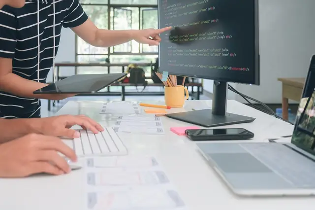 Developer pointing at code on a monitor while working on laptop