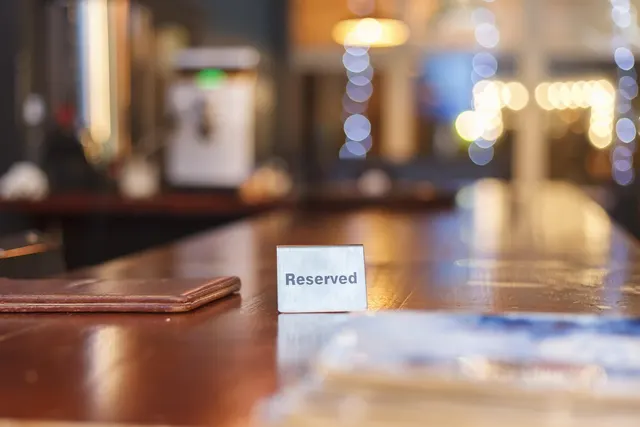 Polished wooden bar counter with a metal Reserved sign and leather check presenter, warm blurred lights behind