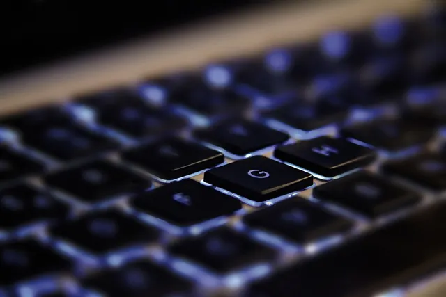 Close-up of a backlit black laptop keyboard with the G key in sharp focus and surrounding keys blurred