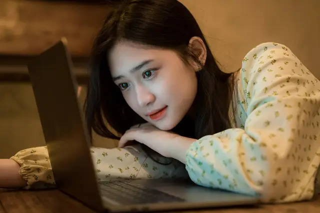 Young woman resting her head on her arms watching a laptop