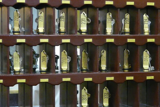 Brass hotel room key fobs numbered 229 to 332 hanging in a dark wooden pigeonhole key rack behind a front desk