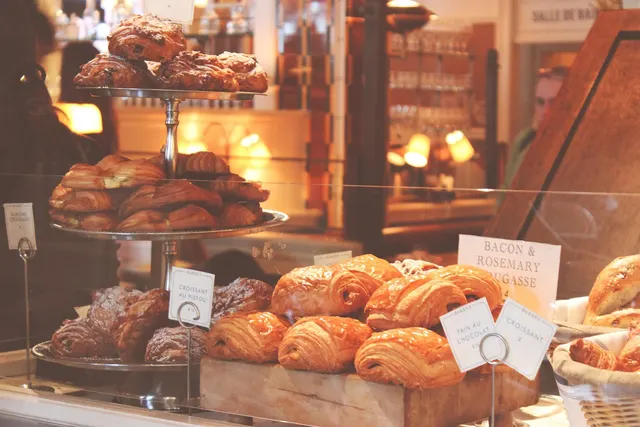 Bakery counter displaying croissants, pain au chocolat and fougasse on tiered stands and wooden crates with handwritten tags