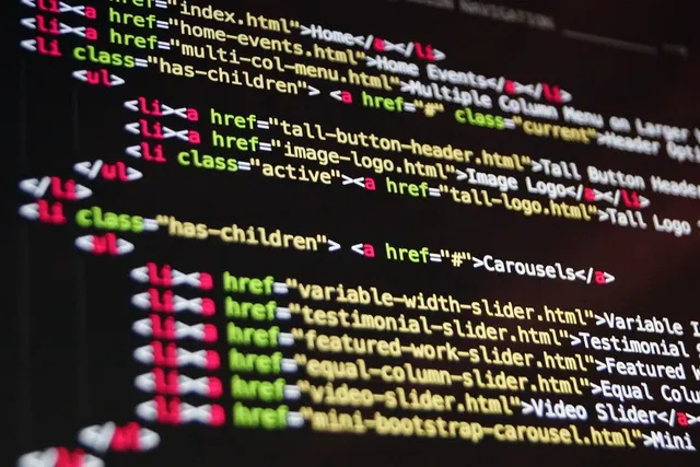 Angled close-up of a dark monitor showing color-coded HTML code for a website navigation menu with list items and links